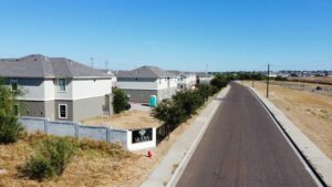 A clear view of a paved road stretching into the distance, bordered by greenery on both sides with La Joya Apartments Monumental Signage