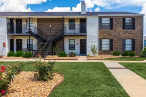 Exterior view of a two-story apartment building at Edgewater Pointe in Biloxi, MS, featuring a mix of brick and siding, a black metal staircase, and landscaped grounds under a blue sky.