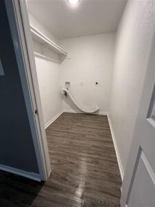 Spacious laundry room with washer and dryer hookups, wood-style flooring, and built-in shelving at Trailwood Village Apartments in Kingwood, TX.