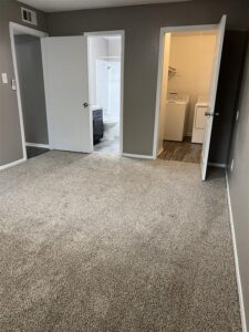 Primary bedroom at Trailwood Village Apartments in Kingwood, TX, featuring plush carpeting, ensuite bathroom, and dedicated laundry room with washer and dryer.