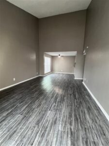 Spacious renovated living room at Trailwood Village Apartments in Kingwood, TX, featuring vaulted ceilings and grey wood-style flooring.
