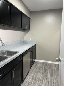 Modern kitchen in a Trailwood Village apartment featuring black shaker-style cabinets, grey granite-look countertops, and stainless steel dishwasher.