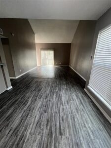 Spacious apartment living room in Kingwood, TX, featuring vaulted ceilings, dark wood-style flooring, and a sliding glass door for natural light.