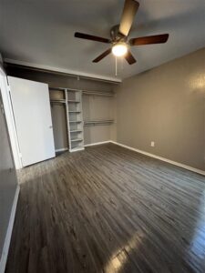Bedroom in a 3-bedroom Abberly unit at Trailwood Village Apartments featuring a built-in closet organization system, wood-plank flooring, and a ceiling fan.