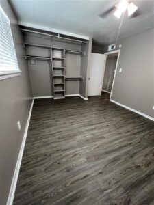 Spacious bedroom in a 3-bedroom Abberly unit at Trailwood Village featuring wood-plank flooring and a built-in closet organization system.