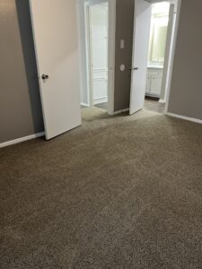 View of a modern master bedroom with plush carpet leading to a walk-in closet and ensuite bathroom at Trailwood Village Apartments in Kingwood, Texas.
