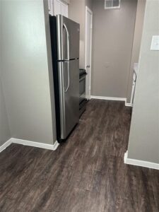Renovated galley kitchen at Trailwood Village Apartments in Kingwood, Texas, featuring stainless steel appliances and dark wood-style plank flooring.